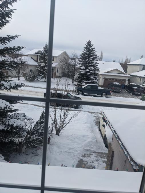 Photograph taken from inside of a window, looking out onto a snow-covered street.