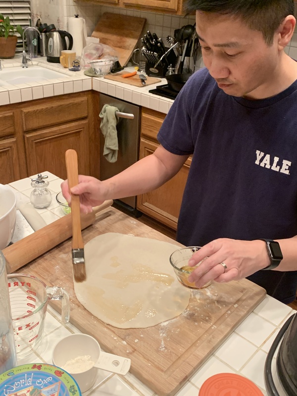 This is a picture taken of a man in his kitchen who is brushing some dough with a kind of oil. 