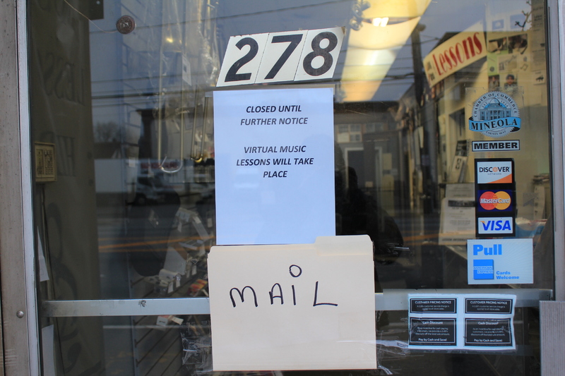 A music store window door with a sign that says "Closed until further notice. Virtual music lessons will take place" and a manilla folder attached underneath with the word mail on it. 