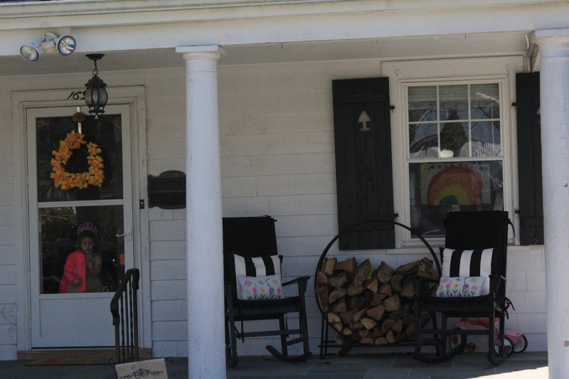 A residential house with a little girl standing behind the screen door, and a rainbow on the front window. 