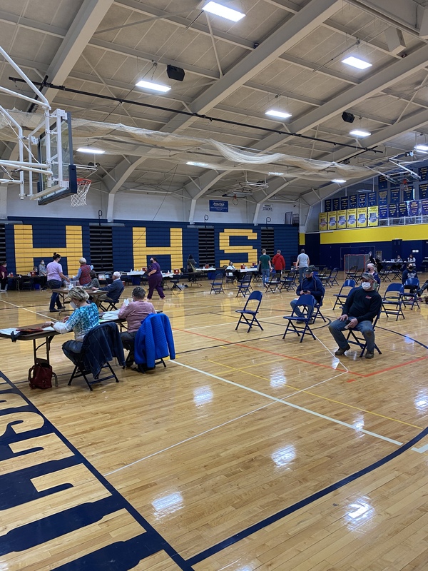 This is a picture of a vaccination center that has been set up inside what appears to be an high school gymnasium. 