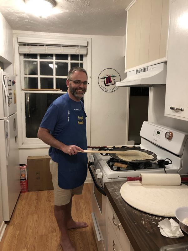 This is a picture of a man smiling while he cooks dough in a skillet in a kitchen. 