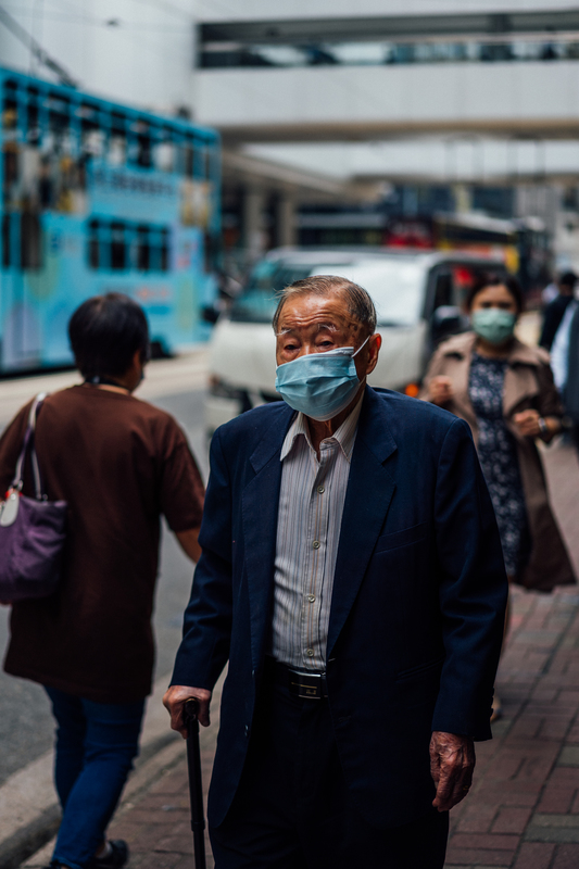 An old man with a walking stick and a mask on. 