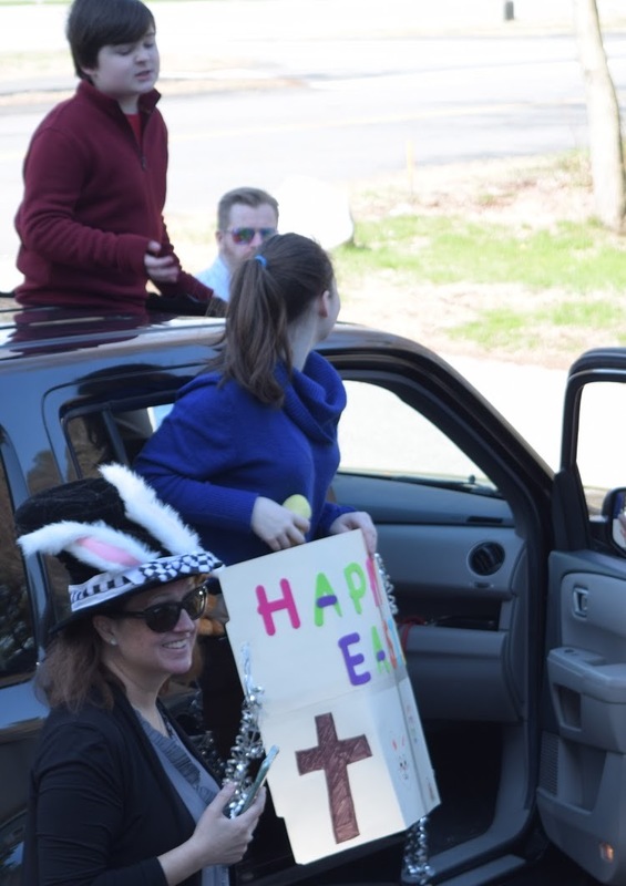 Adults and children around a black vehicle, a girl is holding a sign that says Happy Easter. 