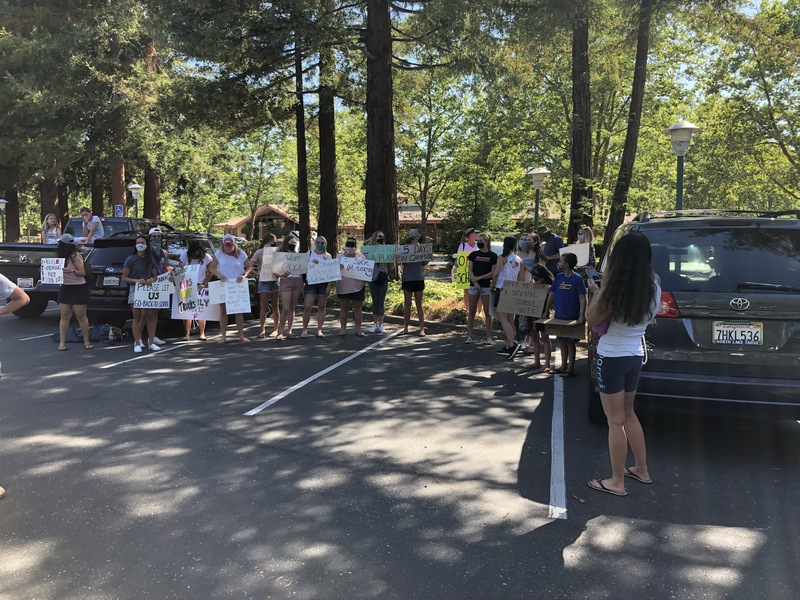 This is a picture taken of a group of people holding signs and protesting in a parking lot. 