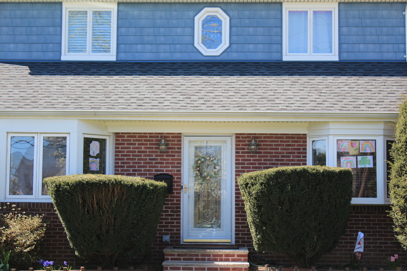 Rainbow drawings and paintings are on the front windows of the house. The front of the house has a spring wreath on the front door. 