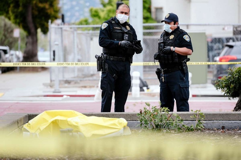 Two police officers are wearing face masks. In front of them is something that is covered with a yellow tarp. 