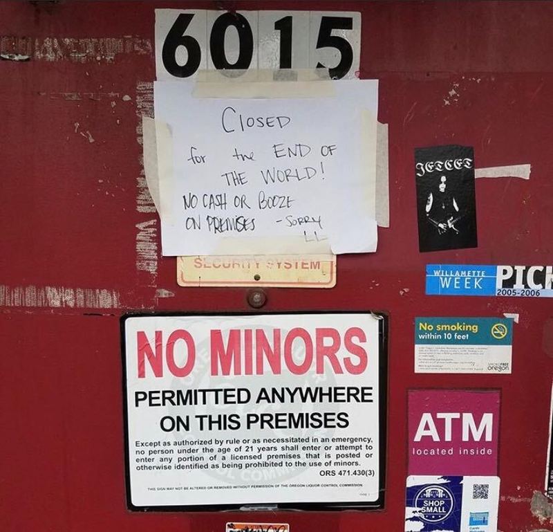 Red door with multiple signs. One signed taped with text, "CLOSED for the END OF THE WORLD! NO CASH OR BOOZE ON PREMISES - SORRY LL" and sign below "NO MINORS PERMITTED ANYWHERE ON THIS PREMISES"