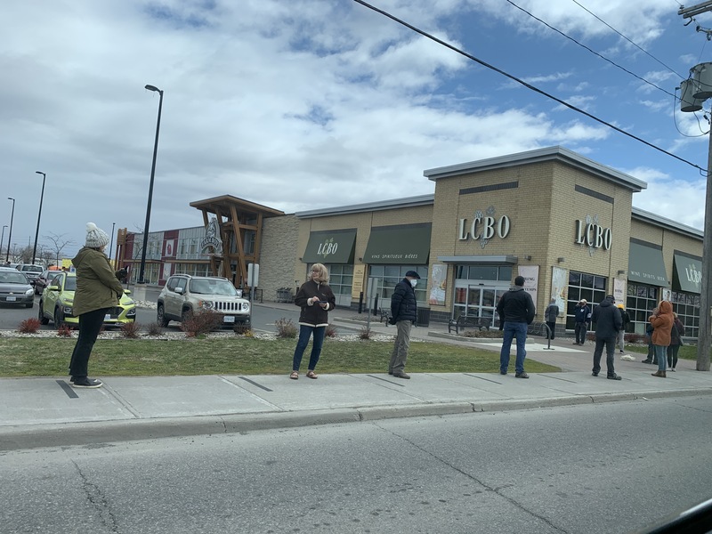 Image of a line of people standing outside social distancing.