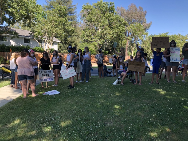 This is a picture taken of a group of people holding signs and protesting. Many are wearing face masks. 