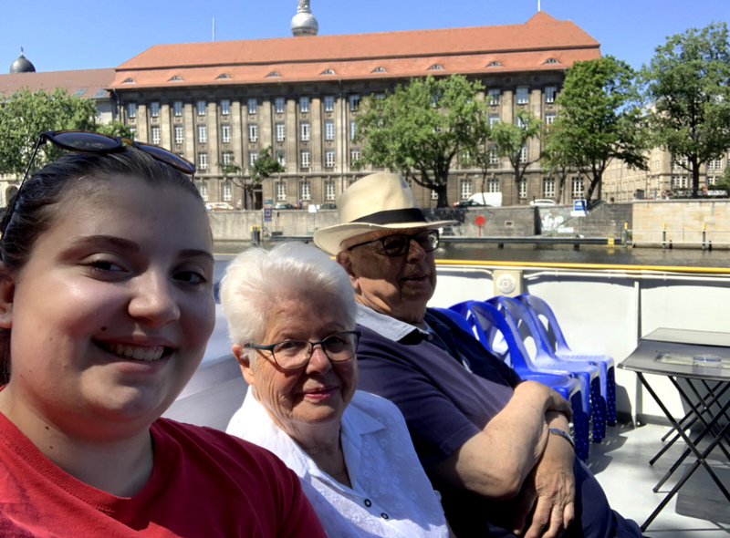 This is a picture taken of three people sitting outside and smiling for a picture. A younger woman is seated next to an older women and an older man. 