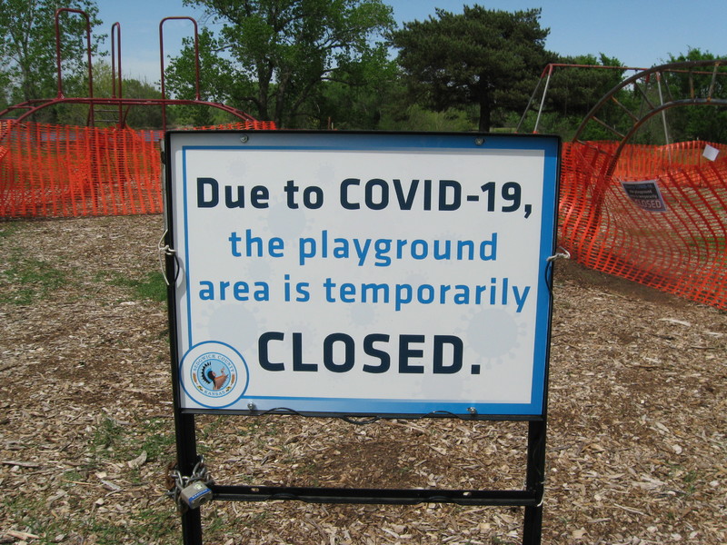 Playground in the background fenced off and sign in front with text, "DUE TO COVID-19, THE PLAYGROUND AREA IS TEMPORARILY CLOSED."