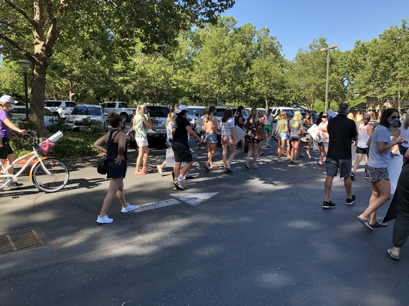 This is a picture taken of a group of people holding signs and protesting while walking down a street. Many are wearing face masks. 