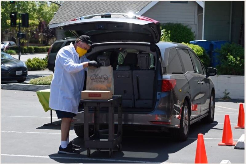 A man in protective equipment providing curbside service at the back of a vehicle.