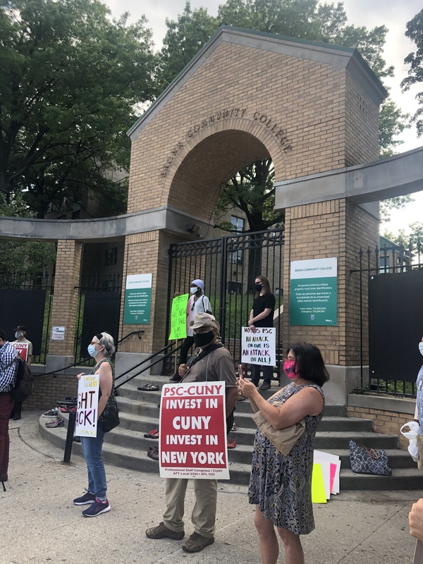 This is a picture of a group of people who are wearing face masks, and protesting outside the gates of a community college. 