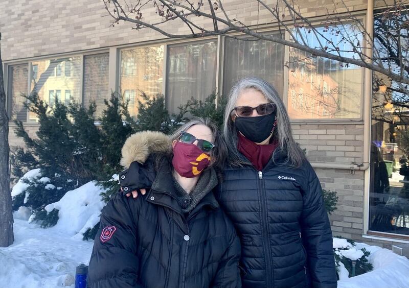 This is a picture of two older women posing side by side for a photo outside. Both are dressed for winter weather, and snow can be seen in the background. 