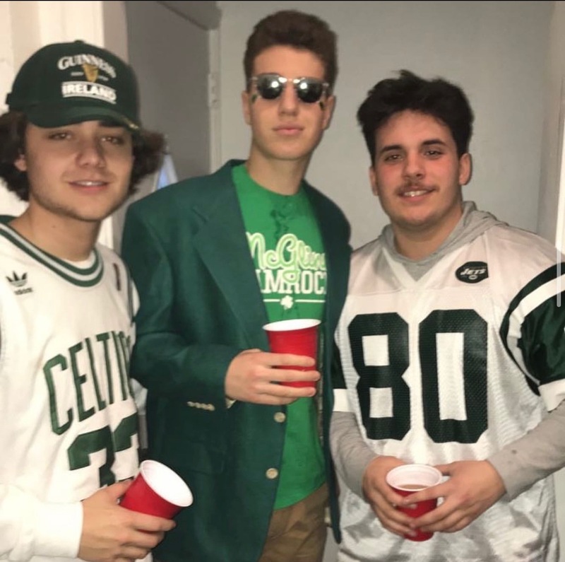 This is a picture of three men in a house wearing sports jerseys and smiling at the camera.  