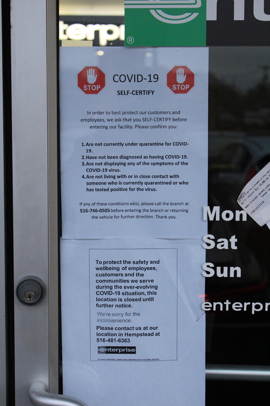 Two signs from Enterprise Car Rental. The first sign says "Stop. COVID-19 self certify. In order to best protect our customers and employees, we ask that you SELF-CERTIFY before entering our facility. Please confirm you:  1. Are not currently under quarantine for COVID-19. 2. Have not been diagnosed as having COVID-19. 3. Are not displaying any of the symptoms of the COVID-19 virus. 4. Are not living with or in close contact with someone who is currently quarantined or who has tested positive for the virus. If any of these conditions exist, please call the branch at 516-746-0505 before entering the branch or returning the vehicle for further direction. Thank you."
The second sign says "To protect the safety and wellbeing of employees, customers and the communities we serve during the ever-evolving COVID-19 situation, this location is closed until further notice. We're sorry for the inconvenience. Please contact us at our location in Hempstead at 516-481-6363. Enterprise" 