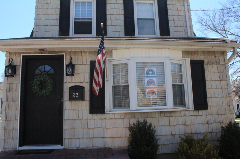 Residential house with three rainbow drawings in the front window. 