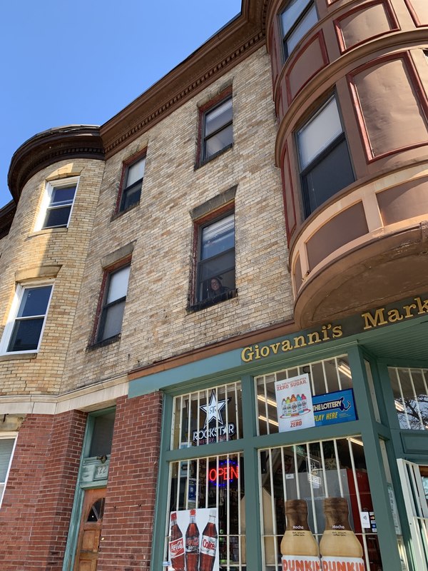 The side of a building has a window open with someone peeking out below their window. 