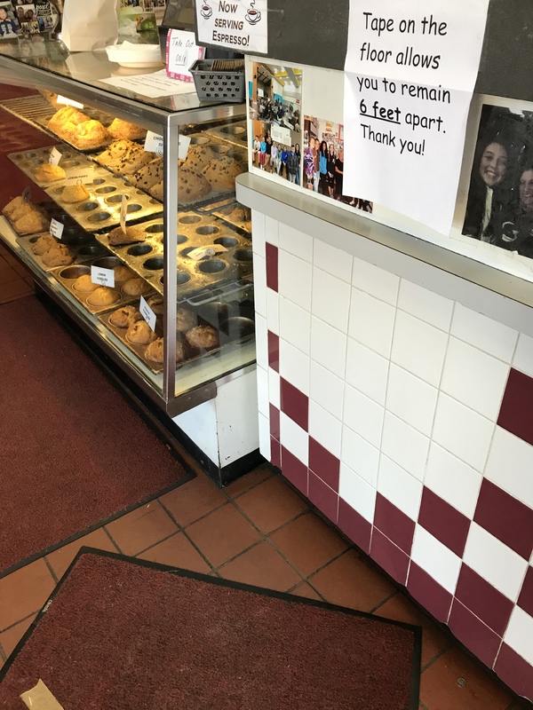 In a store is a display full of muffins and on the floor is tape to follow for social distance. 