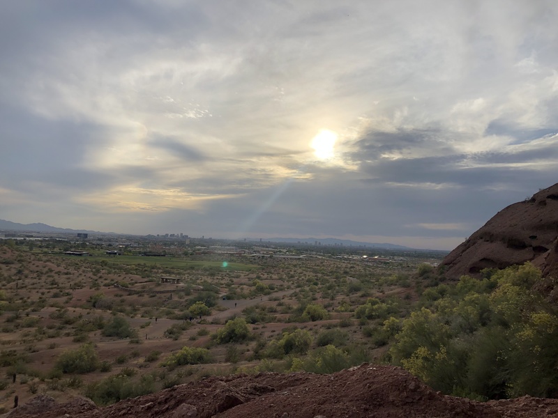 The sun shining through clouds above a desert landscape. 