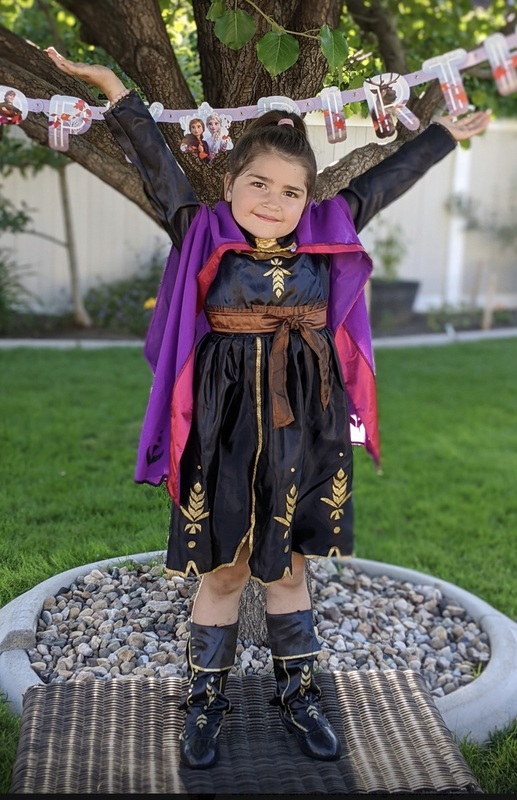 A girl poses in her costume in front of a tree with "Happy Birthday" banner.