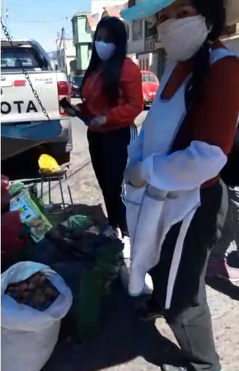 This is a picture of two women standing outside by a table, both wearing masks. 