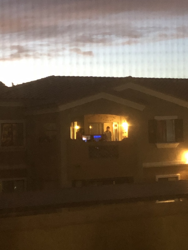 Apartment balcony at night with a lit television. A man is standing next to the television set.