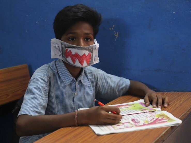 A hand colored mask resembling a shark made out of paper and worn by a child.