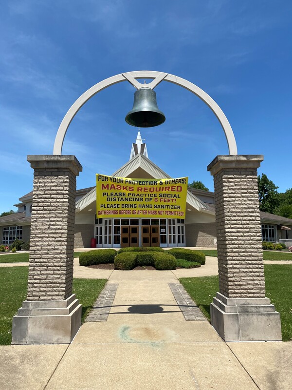 A church sign reading "For your protection and others: Masks Required. Please practice social distancing of 6 feet! Please bring hand sanitizer. Gathering Before or After Mass Not Permitted!".