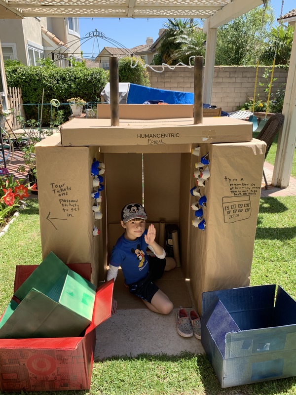 A child sitting in a cover made of cardboard boxes.