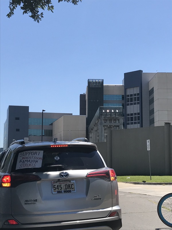 Silver SUV with a sign in the back window with text saying, " Support Whole Foods and Amazon strikes."