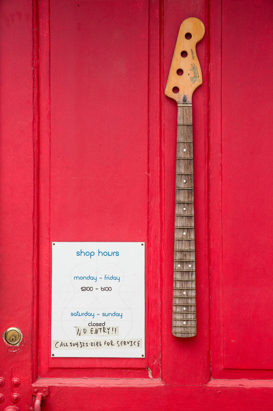 A red front door of Strange Guitarworks with a business hour sign and bass guitar neck.