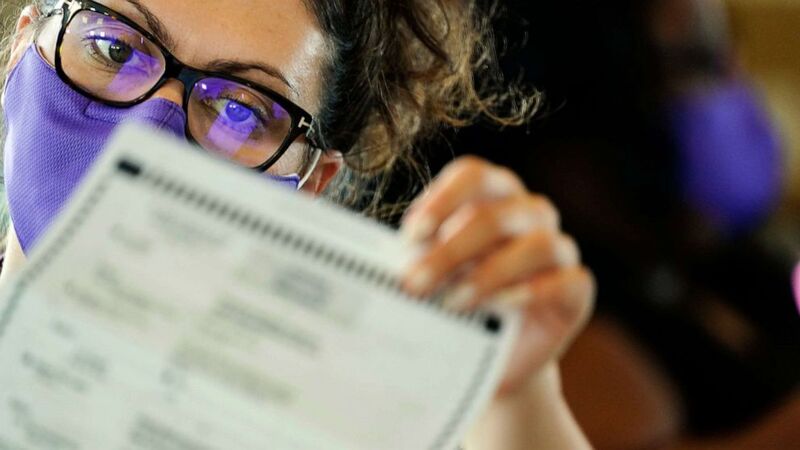 Picture of a female poll worker wearing a mask carefully looking at a document. 