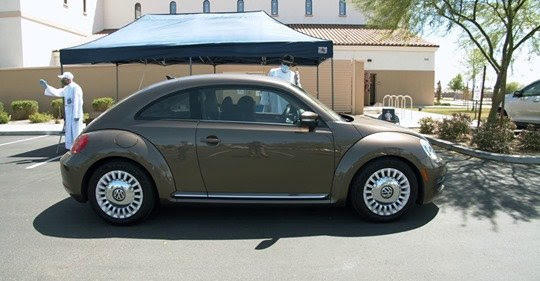 A brown car next to two people and a blue tent. 