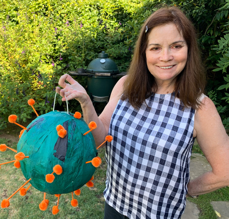 This is a picture taken of a women holding a representation of a COVID-19 germ she made, while standing in a backyard. 