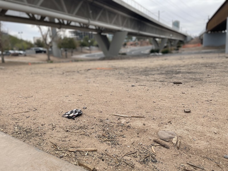 This is a picture of a face mask that has been discarded underneath a bridge in the dirt. 