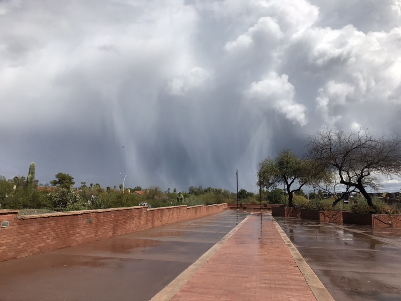 A picture from a distance taken of a rainstorm over a desert landscape.  