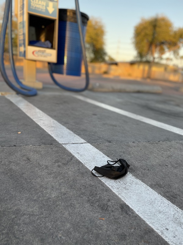 This is a picture of a discarded face mask resting on the ground at what appears to be a gas station. 