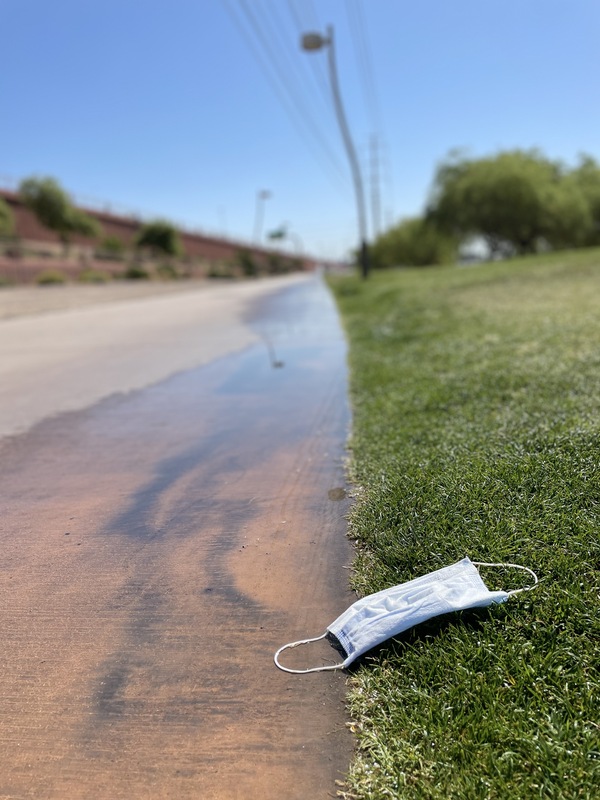 This is a picture of a face mask that has been discarded near a walkway in the grass. 