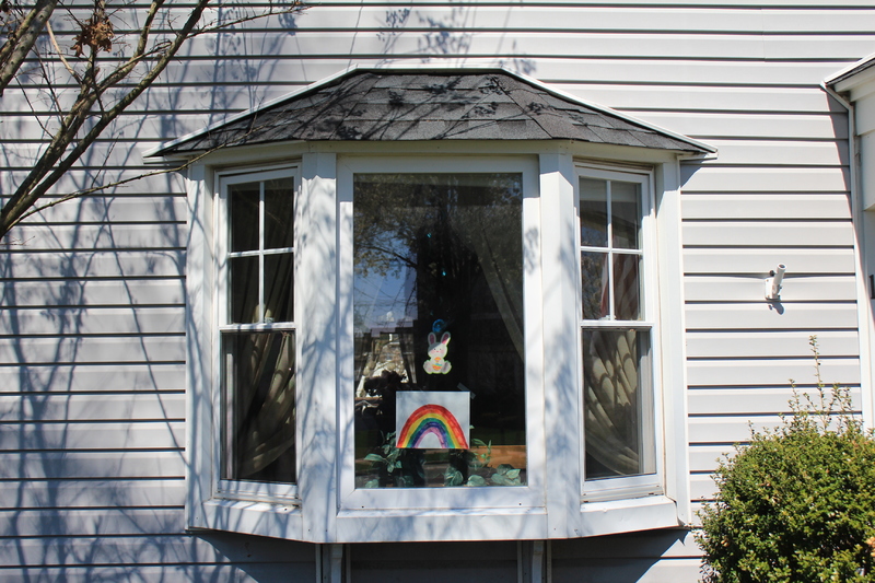 Photograph of a house window that has a rabbit and a rainbow picture taped to it. 