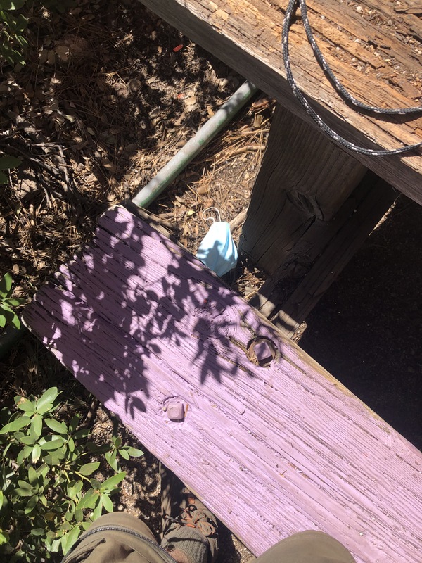 This is a picture of a face mask that has been discarded by a wooden bench outdoors. 