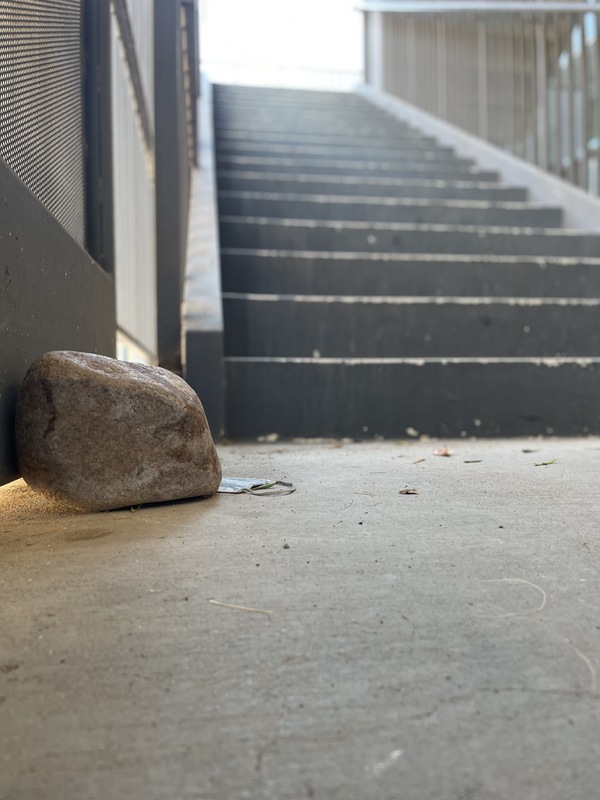 This is a picture of a discarded face mask resting partially behind a large rock on a concrete floor at the base of a stairwell