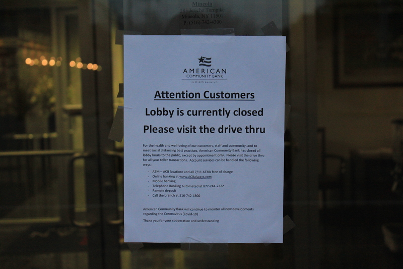 A sign from American Community Bank that says 
"Attention Customers. Lobby is currently closed. Please visit the drive thru. For the health and well-being of our customers, staff and community, and to meet social distancing best practices, American Community Bank has closed all lobby hours to the public, except by appointment only. Please visit the drive thru for all teller transactions. Account services can be handled the follow ways: ATM-ACB locations and all 7/11 ATMs free of charge, online banking at www.ACBalways.com, mobile banking, telephone banking automated at 877-244-7222, remote deposit, call the branch at 516-742-4300. American Community Bank will continue to monitor all new developments regarding the Coronavirus (Covid-19). Thank you for your cooperation and understanding." 