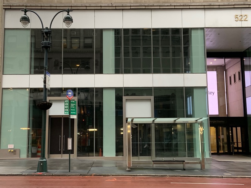 An empty building behind a bus stop and crosswalk. 