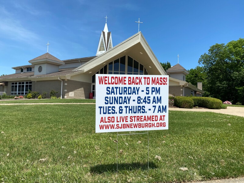 A church yard sign reading "Welcome Back to Mass!" along with the service schedule and an online link to a livestream. 