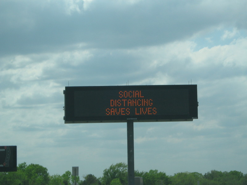 Highway sign with text saying, "SOCIAL DISTANCING SAVES LIVES"