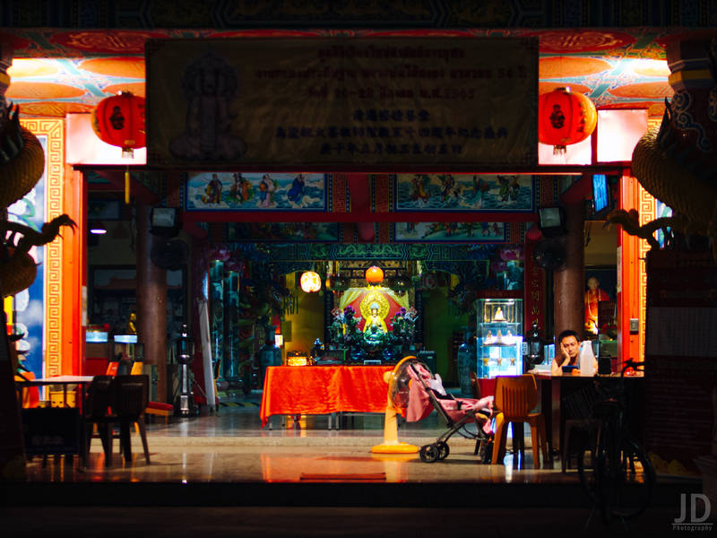 A security guard sits at a desk in an empty room, to the left of him is a child sleeping in a stroller. 