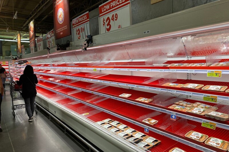 This is a picture taken of several shoppers wearing face masks scouring the mostly empty shelves of the meat department in a grocery store.